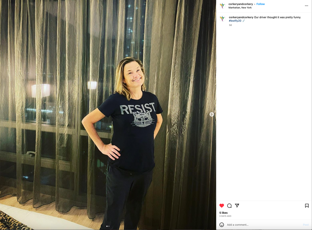 A smiling woman stands with her hands on her hips wearing a union-made, navy blue t-shirt that features the word RESIST above a graphic of a cat’s face.