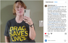 A woman taking a mirror selfie wearing a charcoal t-shirt with the yellow text DRAG SAVES LIVES.