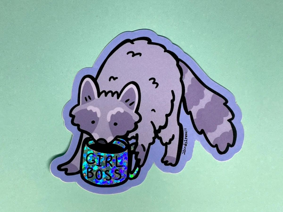 A cartoon raccoon holding a glittery, holographic mug that says GIRL BOSS on a waterproof vinyl sticker.