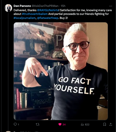 A man with glasses pointing at his union-made black t-shirt that says GO FACT YOURSELF.