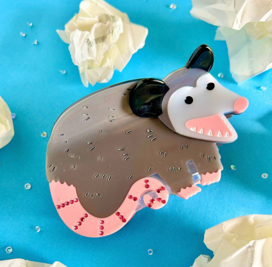 Eco-friendly cellulose acetate hair claw clip shaped like an opossum, featuring a grey body, white face, and a pink tail accented with small red stones.