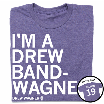 A folded heather purple t-shirt with left-aligned white text that reads "I'M A DREW BAND-WANGER" above smaller text that says, "DREW WAGNER" with a small outline of Illinois that has 19 in its center. A circle image in the bottom right corner shows the back of the t-shirt printed like a jersey with "WAGNER" above 19.
