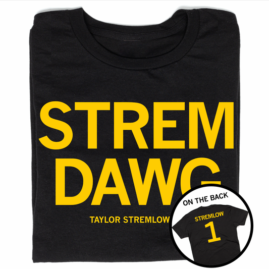 A folded black t-shirt with centered yellow ink text that says, "STREM DAWG" over "TAYLOR STREMLOW" in smaller text. A circle image to the bottom right shows the back of the shirt printed like a jersey with "STREMLOW" over the number 1.