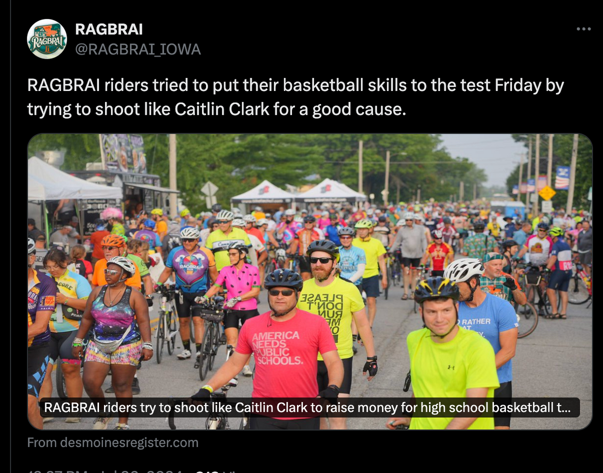 A crowd of cyclists in biking gear gather on a street for a public education charity event, with some participants standing near a basketball hoop to shoot baskets while wearing union made t-shirts.