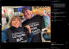 A man and a woman stand inside a store, holding up a union made black t-shirt that reads, Just another member of the Lutheran crime syndicate.