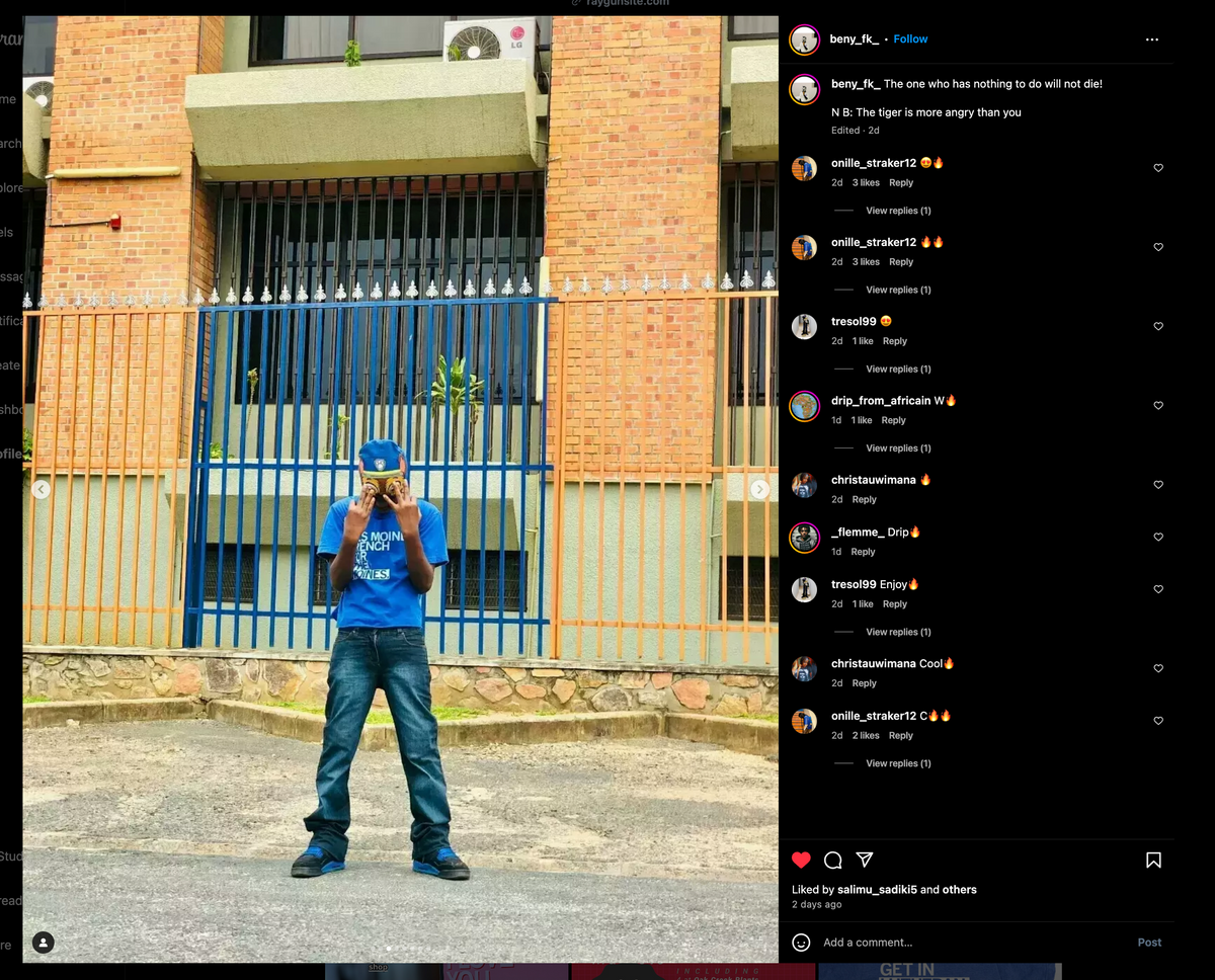 A person in a royal blue T-shirt, jeans, and a blue cap holds a golden tiger mask to their face, standing in front of a blue metal fence and a brick building.