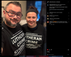 A man with glasses and a woman wearing a headband smile while wearing matching black union-made Lutheran Crime Syndicate t-shirts.