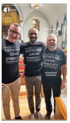 Three men in matching union-made black T-shirts that read Lutheran Crime Syndicate stand inside a church.