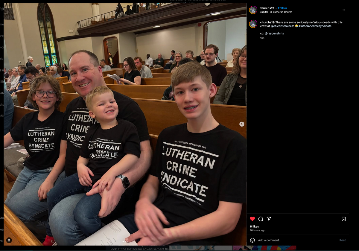 A man sits in a church pew with his three sons, all wearing matching union made black t-shirts that read Just another member of the Lutheran Crime Syndicate.