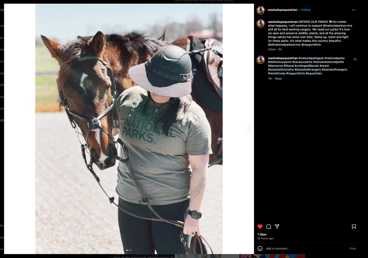 A person wearing a wide-brimmed helmet and a green, eco-friendly T-shirt reading Needs National Parks stands next to a horse wearing a bridle and saddle.