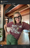 A woman wearing thick black-rimmed glasses and a maroon RAYGUN t-shirt that reads WHAT THE HELL IS GOING ON HERE? stands with her hand on her hip.