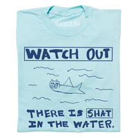 A folded pastel blue t-shirt with royal blue print. A doodle of a shark/cat hybrid is in the center with text above and below that reads "Watch Out. There is a Shat in the water." This shirt was designed by a kid taking part in a contest at our Cedar Rapids store.