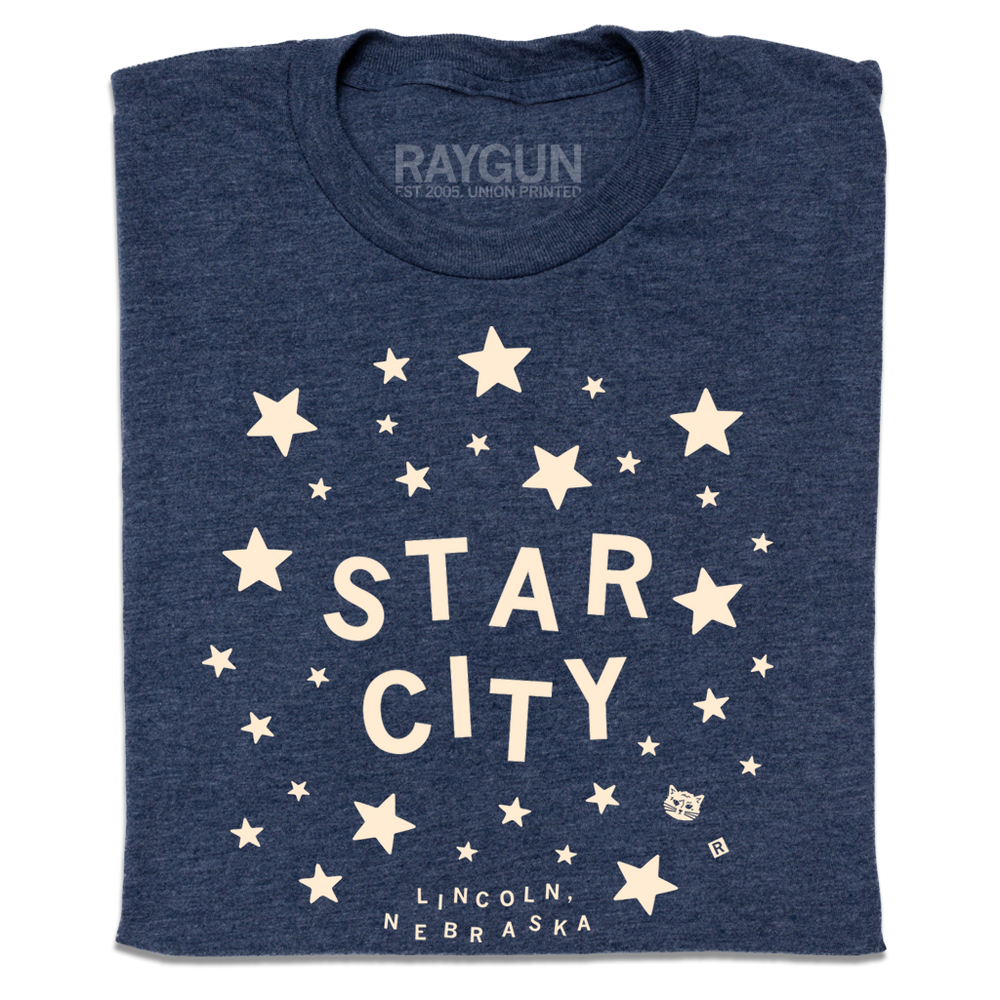 A folded heather navy t-shirt with glow in the dark ink that reads "Star City. Lincoln, Nebraska" surrounded by stars.
