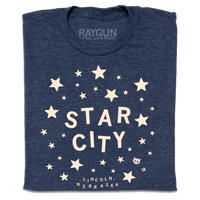 A folded heather navy t-shirt with glow in the dark ink that reads "Star City. Lincoln, Nebraska" surrounded by stars.