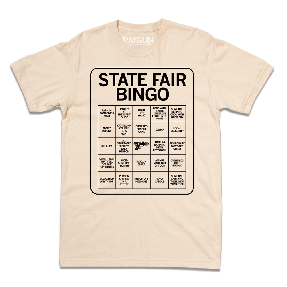 Short sleeve cream shirt with black print illustrating a bingo card. All caps text at the top of the card says, "State Fair Bingo" and the squares list things like "injury at the giant slide" and "someone napping near livestock."
