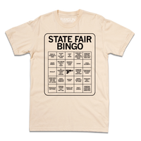 Short sleeve cream shirt with black print illustrating a bingo card. All caps text at the top of the card says, "State Fair Bingo" and the squares list things like "injury at the giant slide" and "someone napping near livestock."