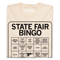 A folded off white shirt with black print depicting a bingo card. All caps text at the top of the card says, "State Fair Bingo" and the squares list things like "injury at the giant slide" and "someone napping near livestock."
