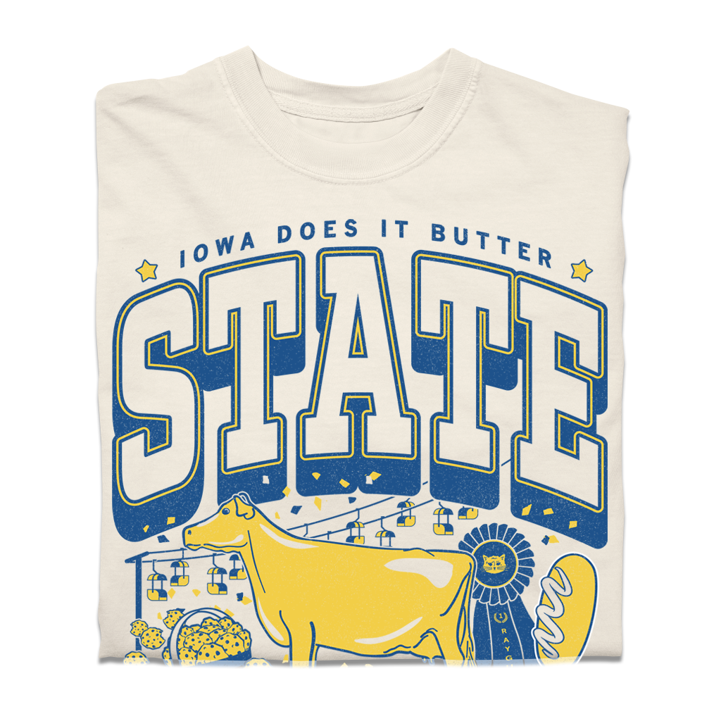 A heavyweight cream-colored t-shirt with a graphic that reads IOWA DOES IT BUTTER and STATE in blue lettering, featuring a yellow cow, a blue ribbon, and a basket of food.