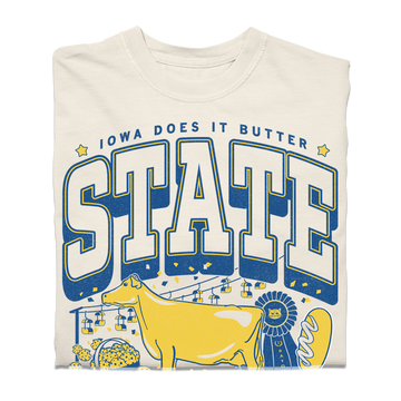A heavyweight cream-colored t-shirt with a graphic that reads IOWA DOES IT BUTTER and STATE in blue lettering, featuring a yellow cow, a blue ribbon, and a basket of food.