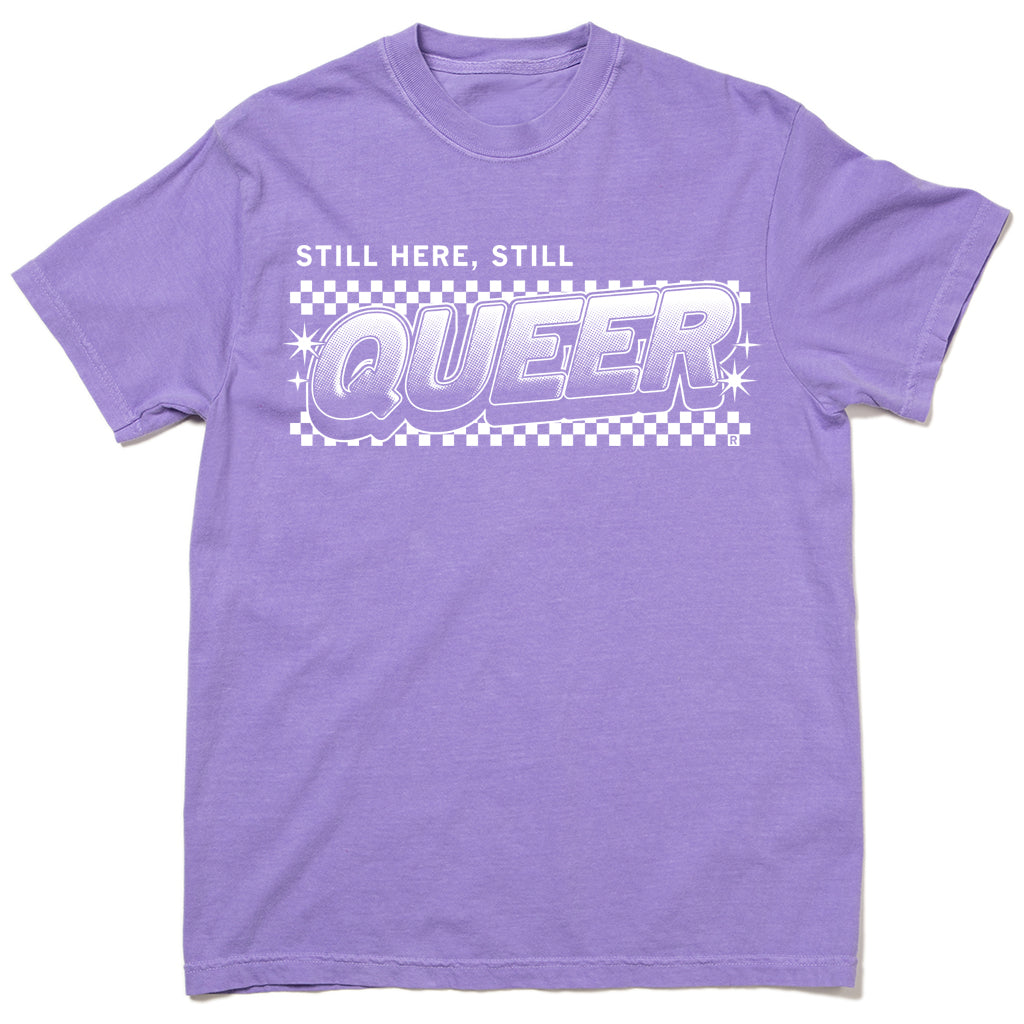 A garment-dyed, purple crew-neck t-shirt featuring a white checkerboard graphic with the text STILL HERE, STILL QUEER in a bold, stylized font.