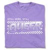 A purple garment-dyed crewneck t-shirt featuring a white STILL HERE, STILL QUEER graphic over a checkered pattern.