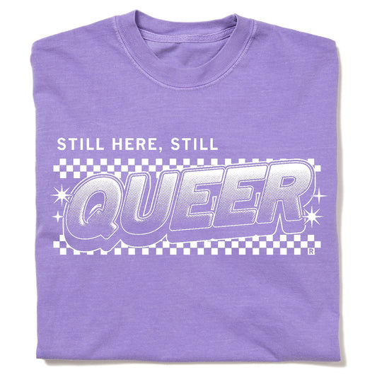 A purple garment-dyed crewneck t-shirt featuring a white STILL HERE, STILL QUEER graphic over a checkered pattern.