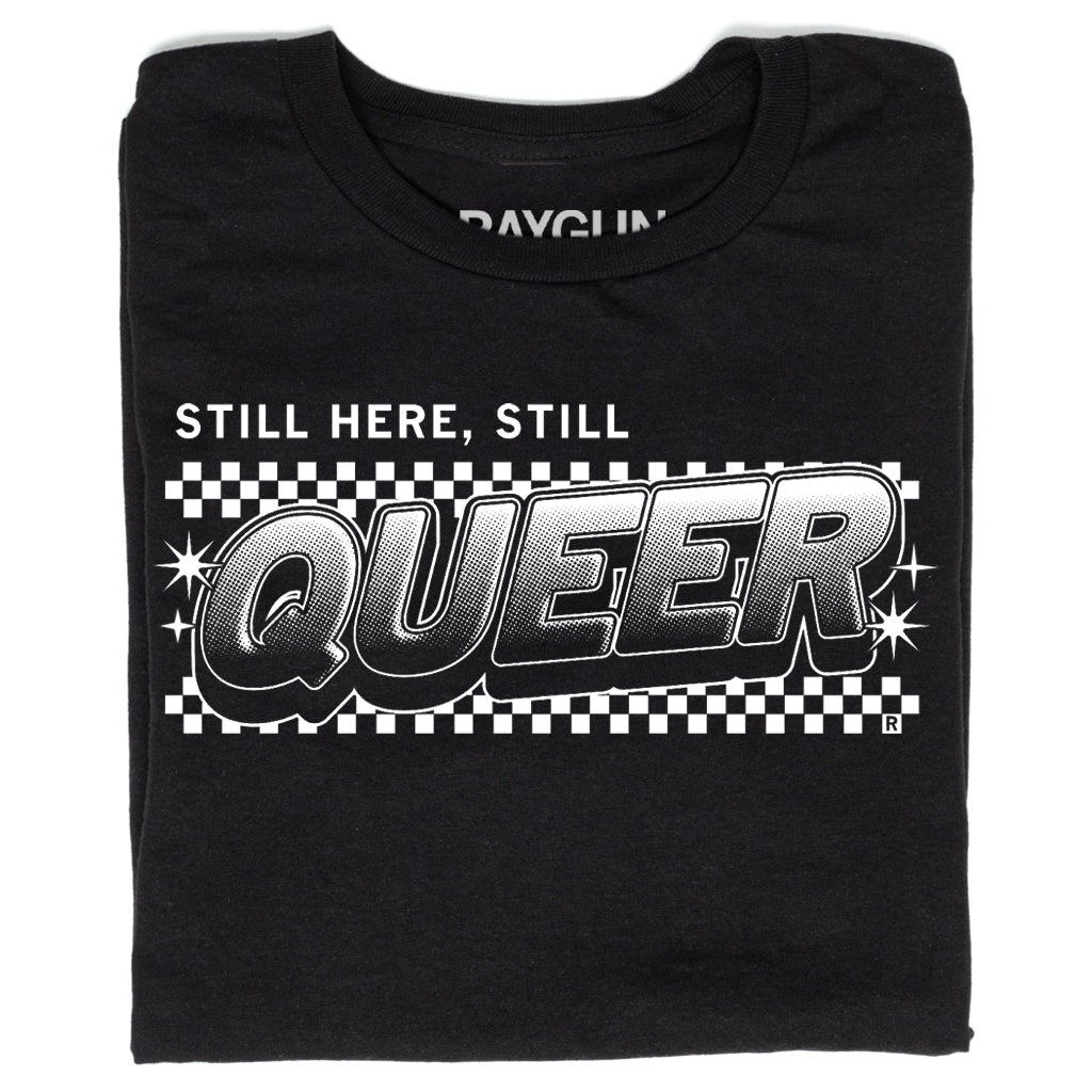 Black, union-made t-shirt featuring the text STILL HERE, STILL QUEER in a bold, comic-style font over a black and white checkerboard background.