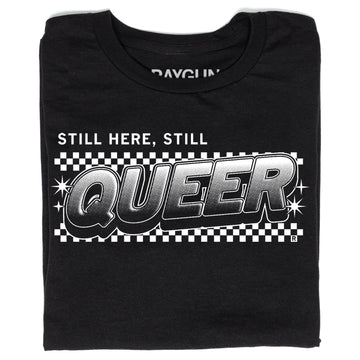 Black, union-made t-shirt featuring the text STILL HERE, STILL QUEER in a bold, comic-style font over a black and white checkerboard background.