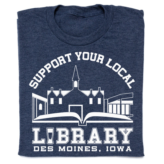 Dark blue RAYGUN t-shirt featuring a white graphic of a library building above an open book and the text SUPPORT YOUR LOCAL LIBRARY DES MOINES, IOWA.