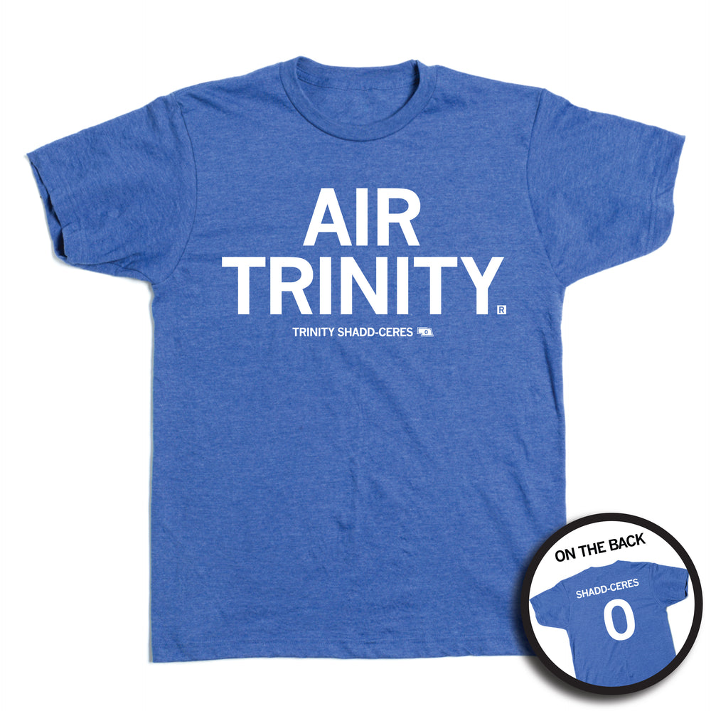 Short-sleeve heather royal blue t-shirt with all caps white text that says, "Air Trinity" in large text with small print below that reads "Trinity Shadd-Ceres." A small outline of Nebraska is printed to the right of her name with the number 0 in it. A small, circle image in the bottom right shows the back print. The back of the shirt is laid out like a jersey with her last name over her number.