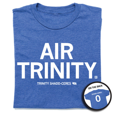 A folded heather royal blue t-shirt with all caps white text that says, "Air Trinity" in large text with small print below that reads "Trinity Shadd-Ceres." A small outline of Nebraska is printed to the right of her name with the number 0 in it. A small, circle image in the bottom right shows the back print. The back of the shirt is laid out like a jersey with her last name over her number.