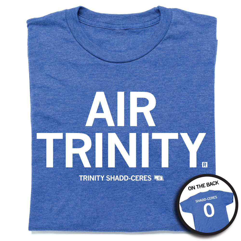 A folded heather royal blue t-shirt with all caps white text that says, "Air Trinity" in large text with small print below that reads "Trinity Shadd-Ceres." A small outline of Nebraska is printed to the right of her name with the number 0 in it. A small, circle image in the bottom right shows the back print. The back of the shirt is laid out like a jersey with her last name over her number.