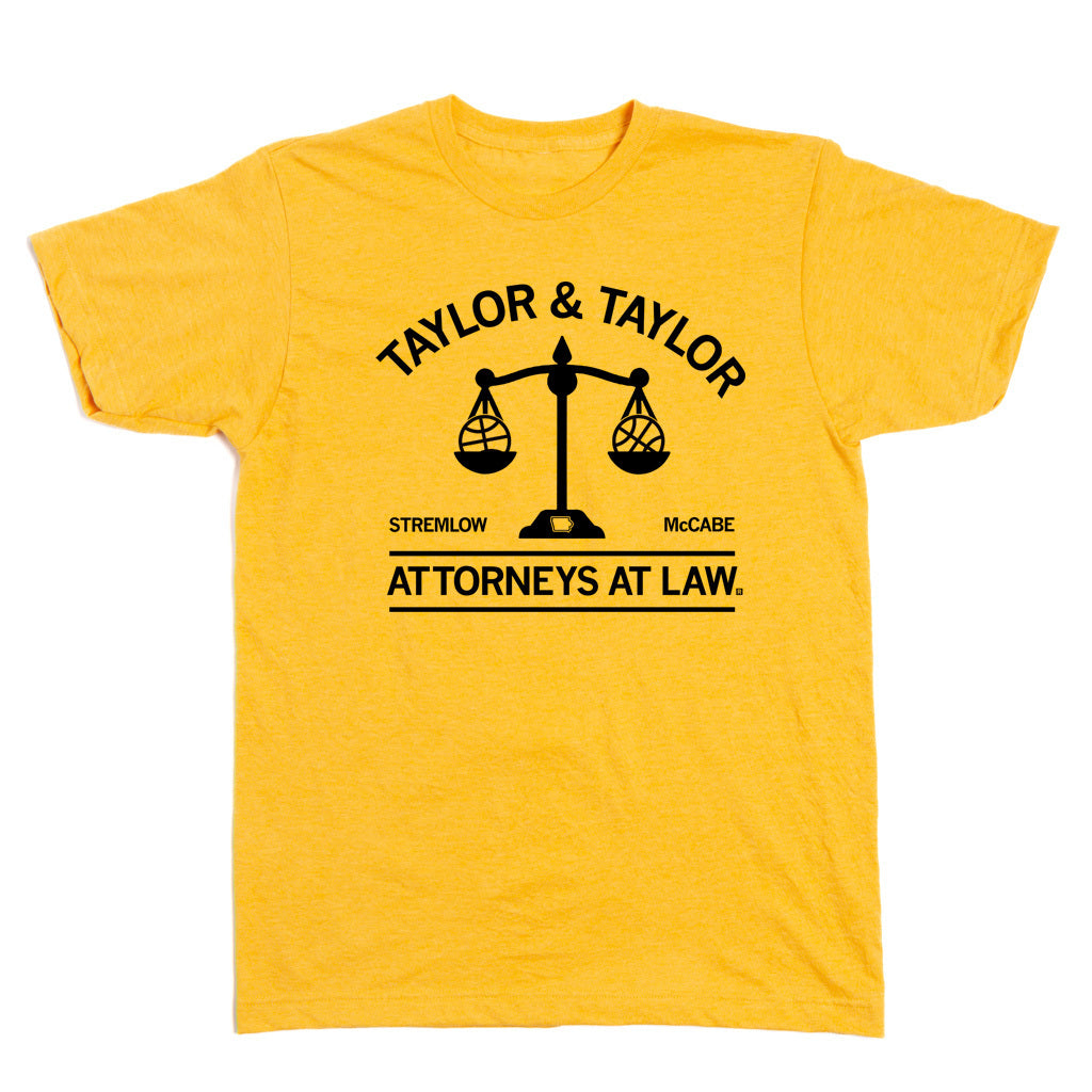 A heather gold shirt with black ink text that reads "Taylor & Taylor: Attorneys At Law" with in image of a scale that has a basketball on either side