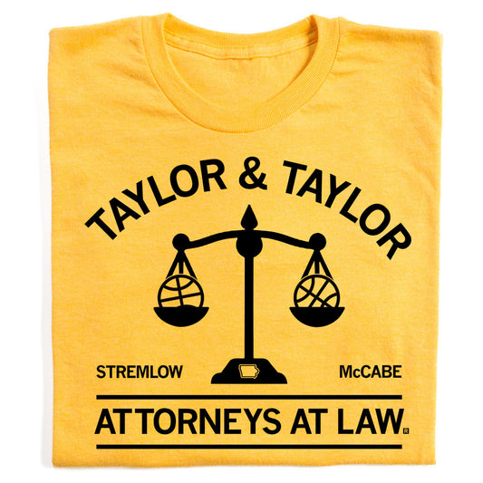Heather yellow t-shirt with black ink that reads "Taylor & Taylor: Attorneys At Law" with in image of a scale that has a basketball on either side