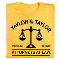 Heather yellow t-shirt with black ink that reads "Taylor & Taylor: Attorneys At Law" with in image of a scale that has a basketball on either side