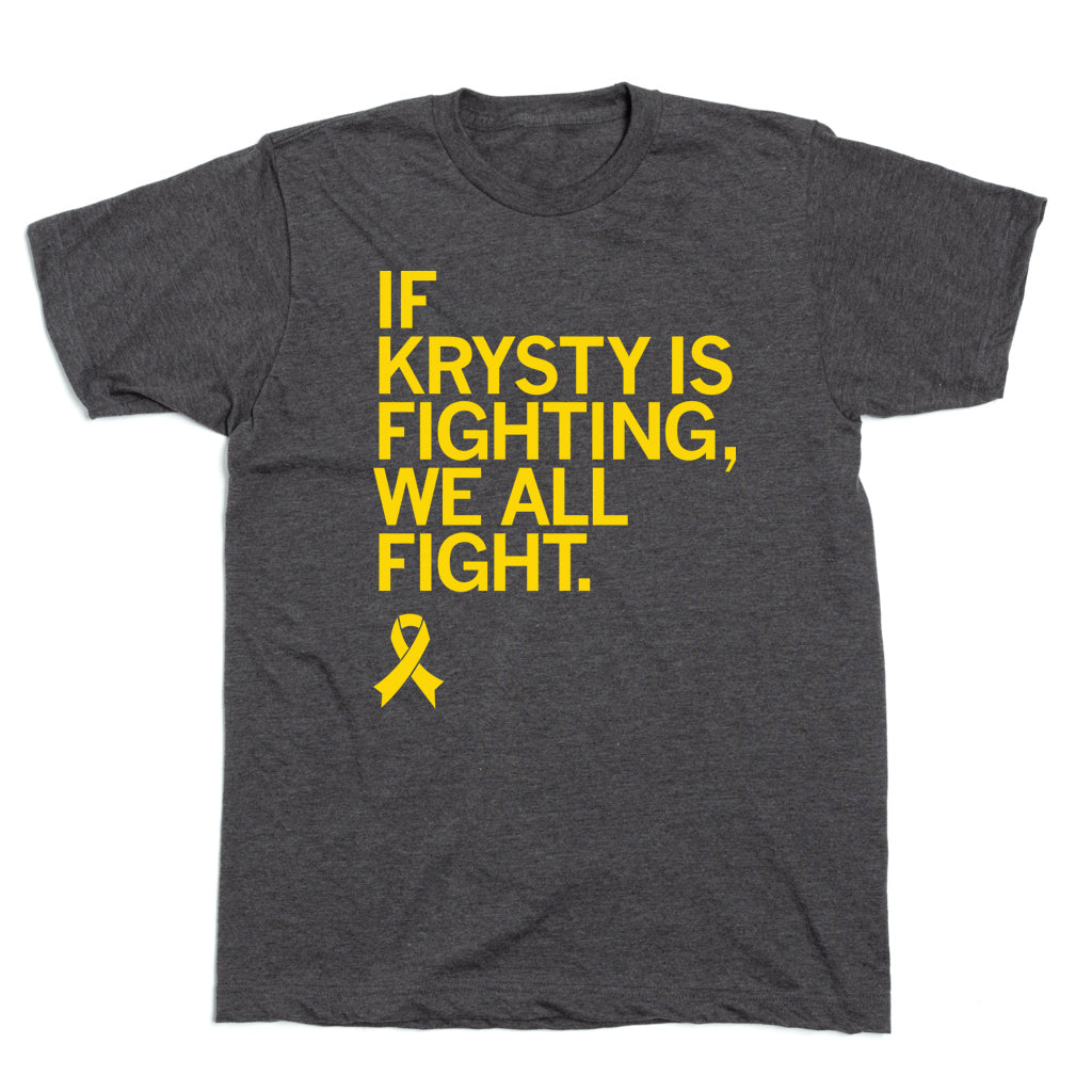 Charcoal T-shirt featuring yellow text that reads, IF KRYSTY IS FIGHTING, WE ALL FIGHT, above a yellow osteosarcoma awareness ribbon.