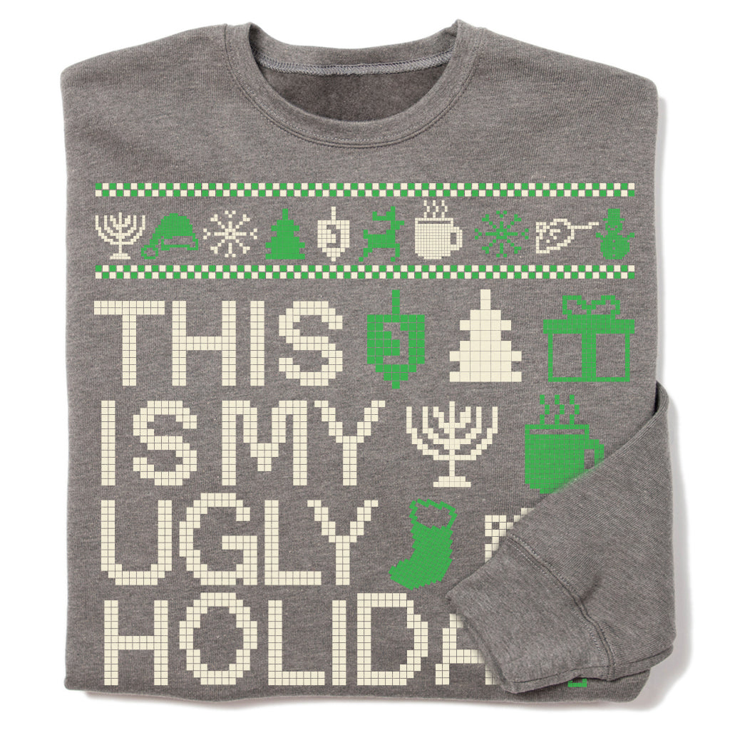 A grey RAYGUN crew sweatshirt featuring the text THIS IS MY UGLY HOLIDA in pixelated letters, surrounded by green and white icons of menorahs, dreidels, trees, and gift boxes.