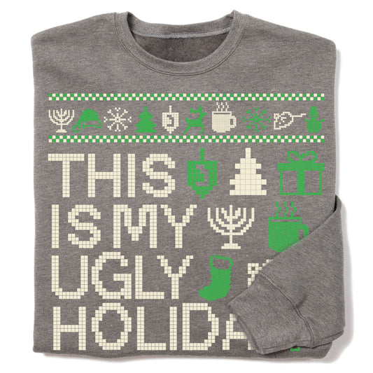 A grey RAYGUN crew sweatshirt featuring the text THIS IS MY UGLY HOLIDA in pixelated letters, surrounded by green and white icons of menorahs, dreidels, trees, and gift boxes.