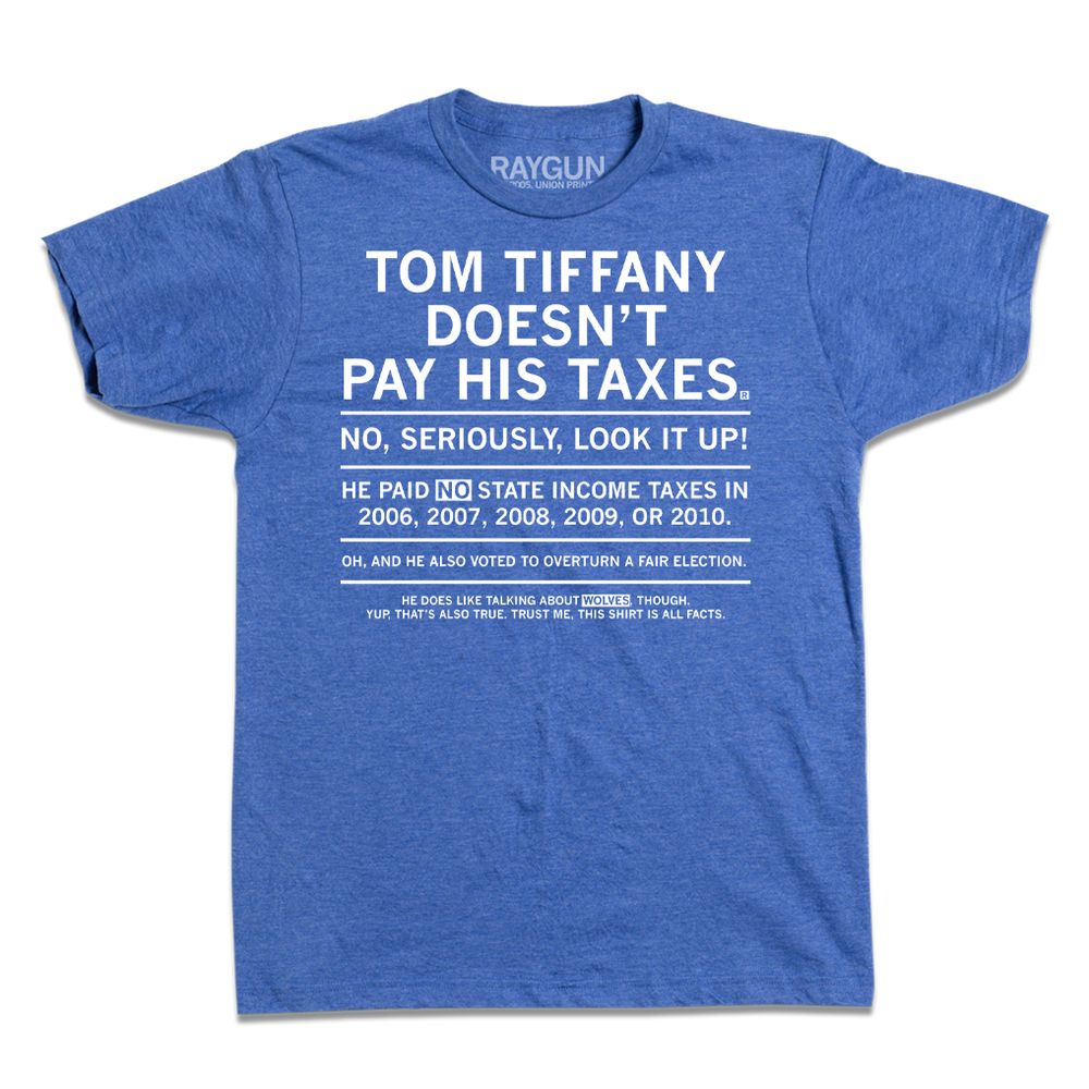 Short sleeve heather blue t-shirt with centered white ink text that gets smaller every sentence. It says, "Tom Tiffany Doesn't Pay His Taxes. No, seriously, look it up! He paid NO state income taxes in 2006, 2007, 2008, 2009, or 2010. Oh, and he also voted to overturn a fair election. He does like talking about wolves though. Yup, that's also true. Trust me, this shirt is all facts."