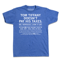 Short sleeve heather blue t-shirt with centered white ink text that gets smaller every sentence. It says, "Tom Tiffany Doesn't Pay His Taxes. No, seriously, look it up! He paid NO state income taxes in 2006, 2007, 2008, 2009, or 2010. Oh, and he also voted to overturn a fair election. He does like talking about wolves though. Yup, that's also true. Trust me, this shirt is all facts."