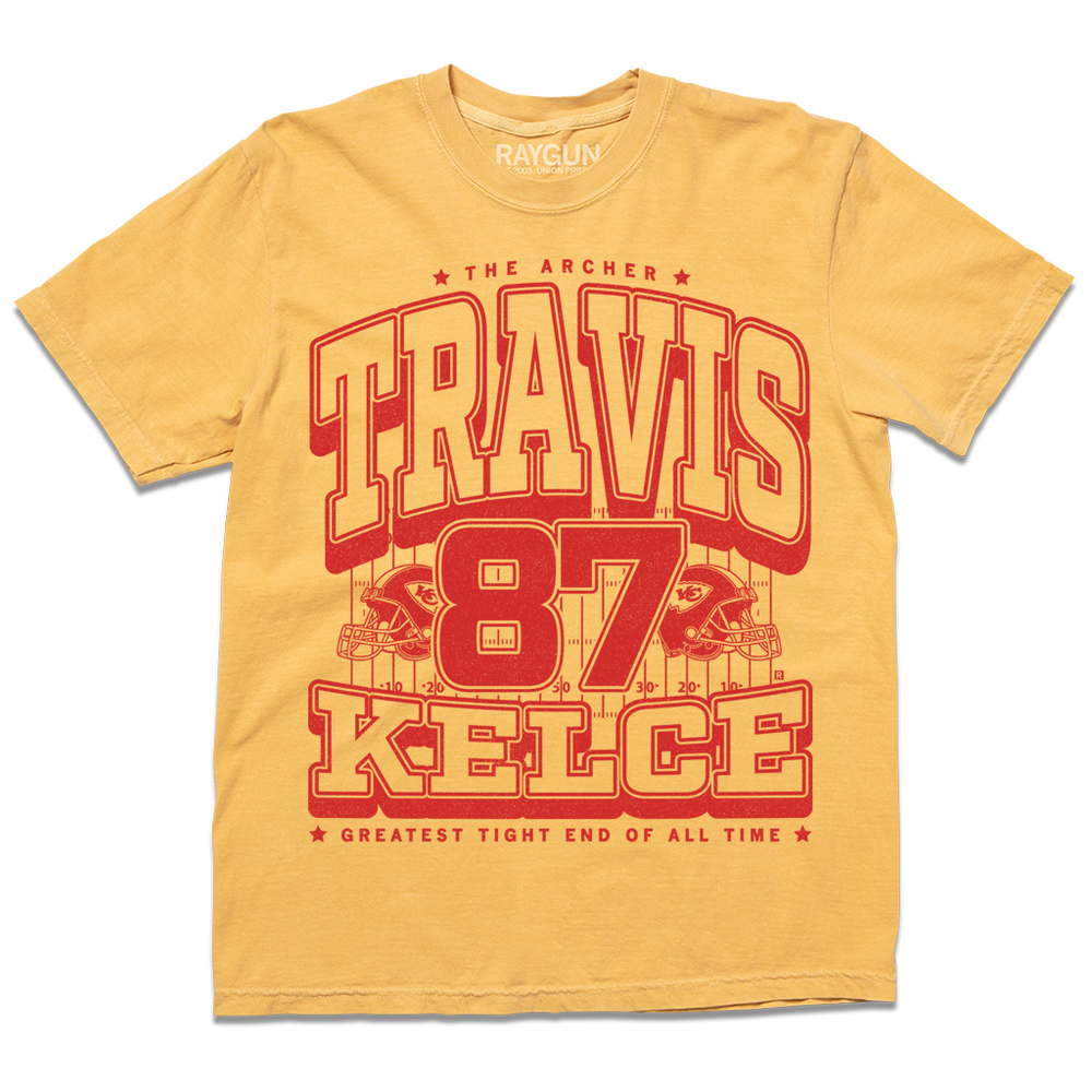 A Yellow shirt with red ink that reads "The Archer. Travis Kelce. The Greatest Tight End Of All Time" over an illustration of a football field  with the number 87 and a football helmet on either side.