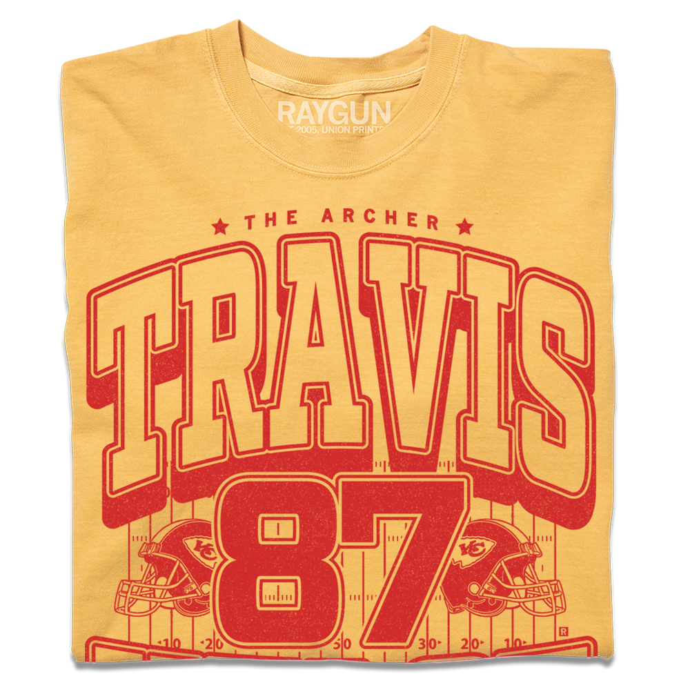 Gold shirt with bright red ink that reads "The Archer. Travis Kelce. The Greatest Tight End Of All Time" over an illustration of a football field  with the number 87 and a football helmet on either side.