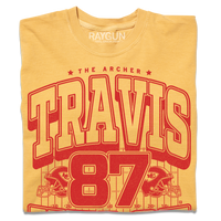Gold shirt with bright red ink that reads "The Archer. Travis Kelce. The Greatest Tight End Of All Time" over an illustration of a football field  with the number 87 and a football helmet on either side.