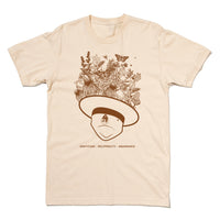 A cream t-shirt with brown ink depicting an upside down park ranger hat with flowers, leaves, birds, and pollinators emerging from it. Text below reads "Gratitude - Reciprocity - Abundance"