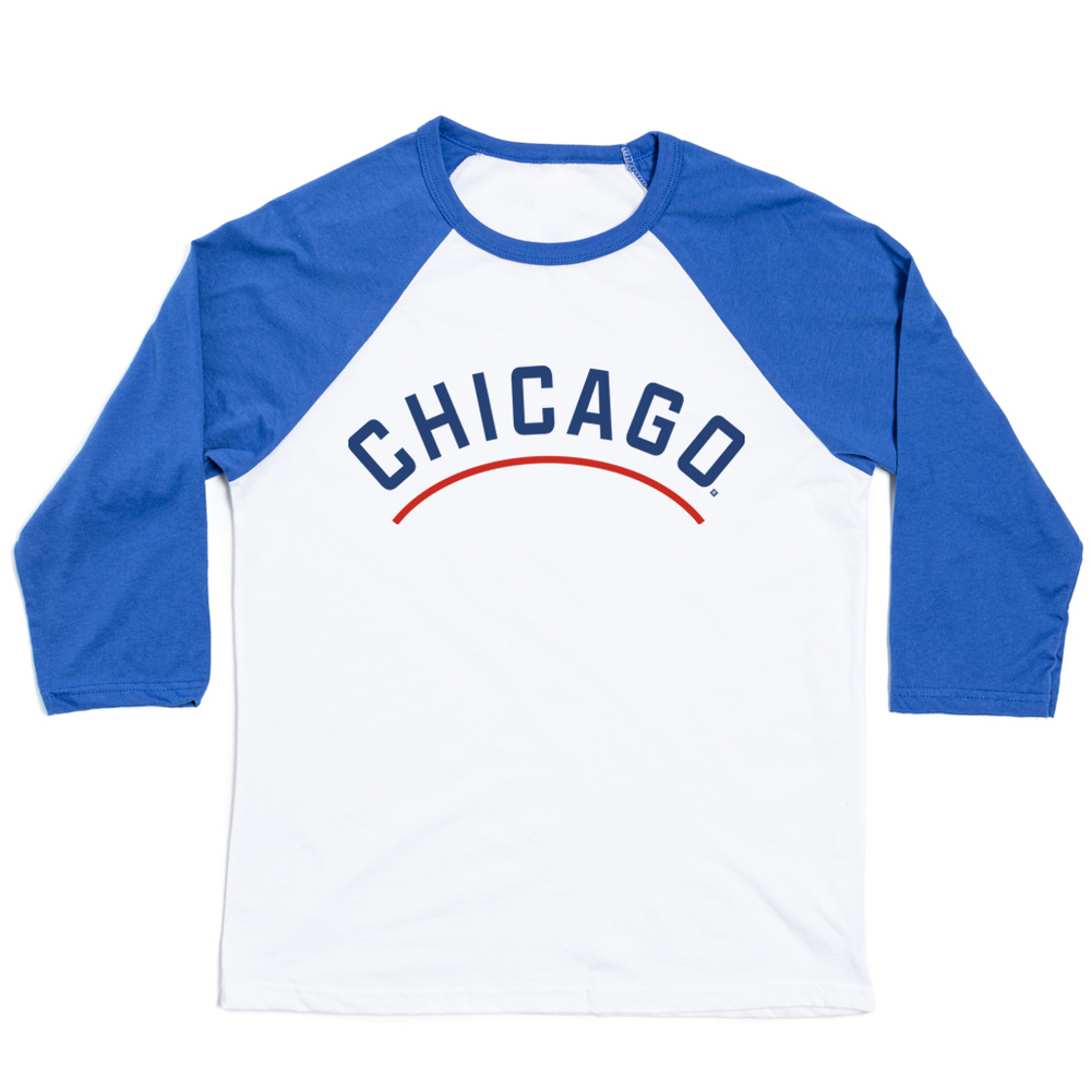 A three quarter sleeve baseball tee with a white body and blue sleeves. "Chicago" is printed in an all caps arch with blue print. Below "Chicago" is a red line.