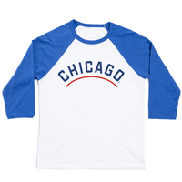 A three quarter sleeve baseball tee with a white body and blue sleeves. "Chicago" is printed in an all caps arch with blue print. Below "Chicago" is a red line.