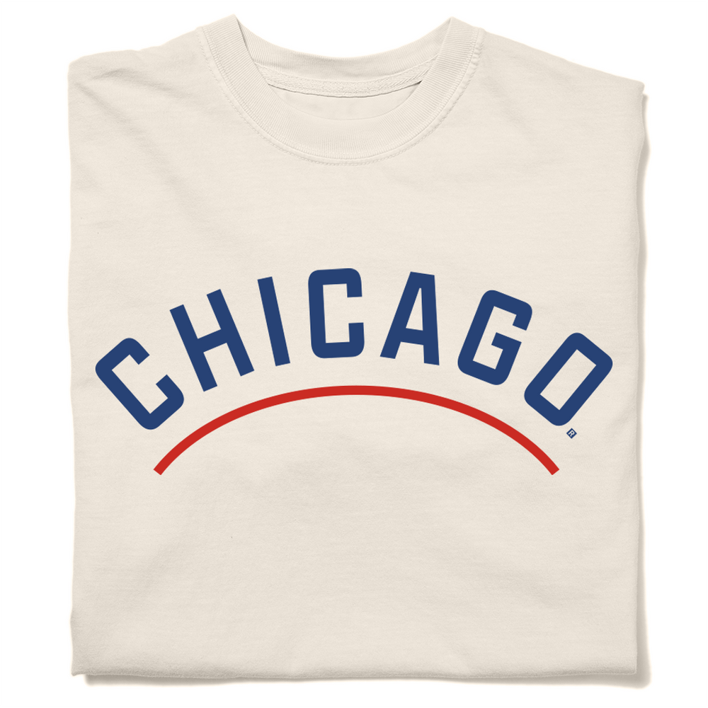 Folded ivory heavyweight t-shirt with "CHICAGO" printed in curved blue font. A red arch is printed below the text, parallel to it.