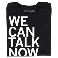 A folded black t-shirt with left-aligned white ink text that reads "We Can Talk Now"