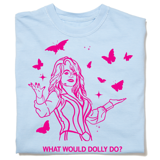 A folded pastel blue heavyweight t-shirt with hot pink ink depicting Dolly Parton with open arms, surrounding by butterflies and sparkles. All caps text below says, "WHAT WOULD DOLLY DO?"