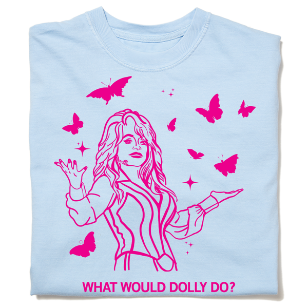 A folded pastel blue heavyweight t-shirt with hot pink ink depicting Dolly Parton with open arms, surrounding by butterflies and sparkles. All caps text below says, 